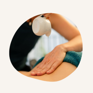 Une main sur le dos reçoit l'huile chaude qui coule depuis un récipient, pour venir jusqu'au dos de la personne massée.